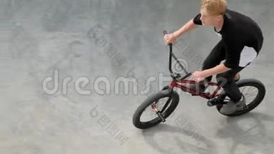 一个男孩正在阳光明媚的日子里在滑板公园骑自行车。 超级慢动作
